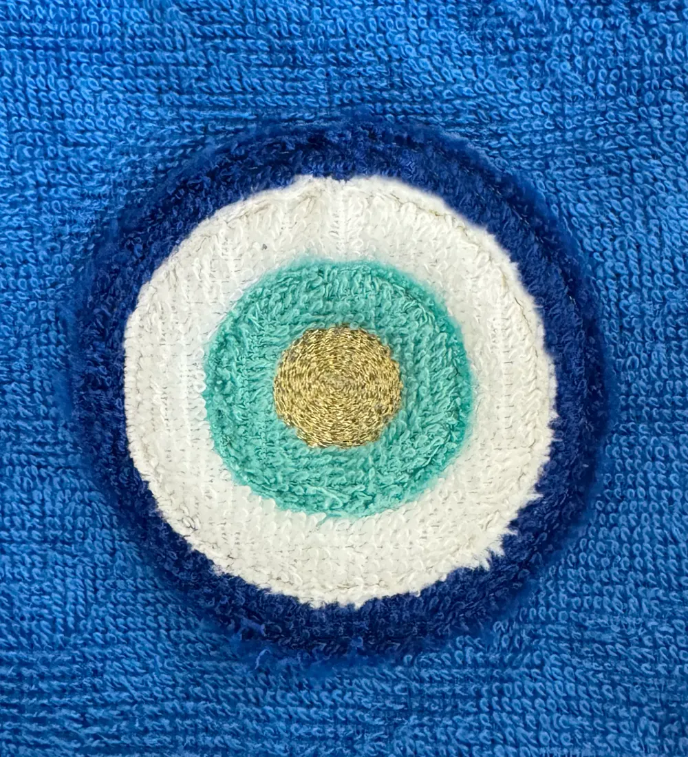 Protective eye in white, turquoise and midnight-blue terry appliqué on blue terry, its centre embroidered in gold thread