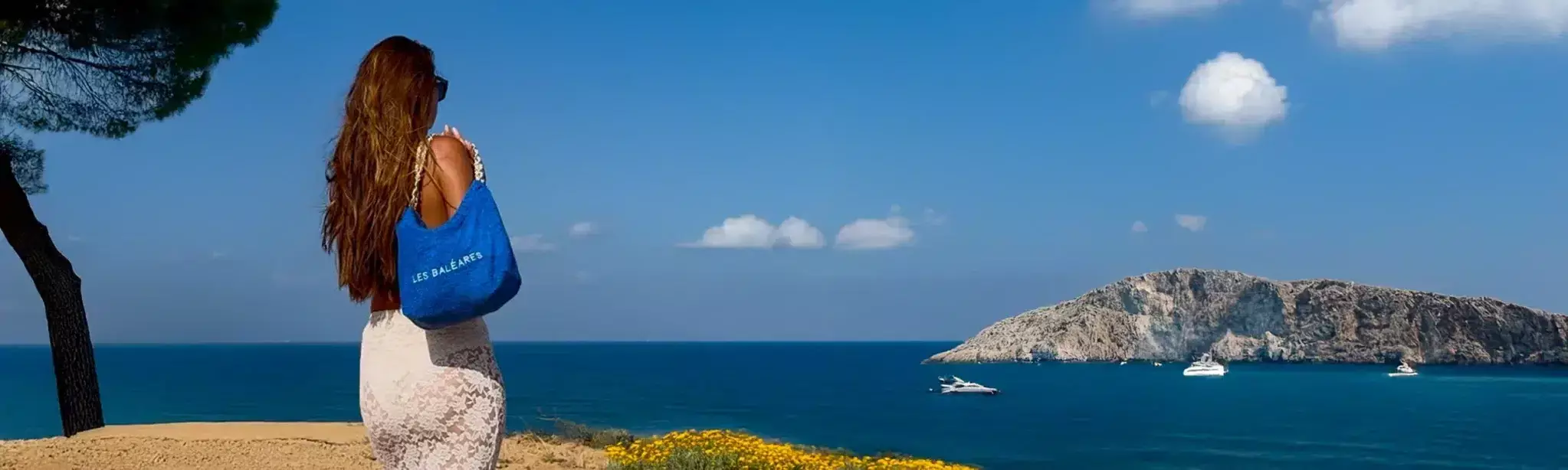 Leslie-Sulman-Beach-Beyond-Collection-26-baleares-10-3 Créatrice Leslie Sulman portant le sac de plage bleu azur brodé Les Baléares face à la mer et yacht, collection luxe Beach and Beyond.