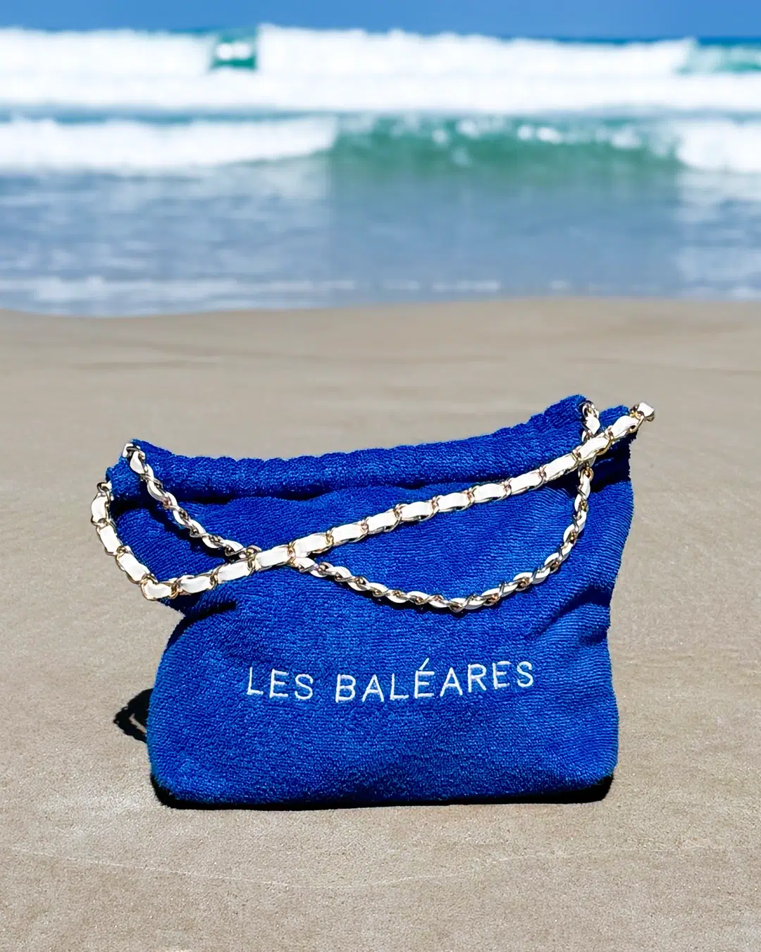 Leslie-Sulman-Beach-Beyond-Collection-26-baleares-royal-blue-3 Sac de plage personnalisé en éponge royal blue brodé du message Les Baléares, posé sur le sable au bord de la mer.